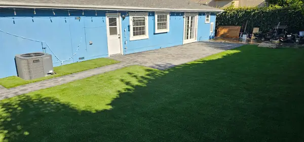 Turf lawn and paver walkway behind a blue house